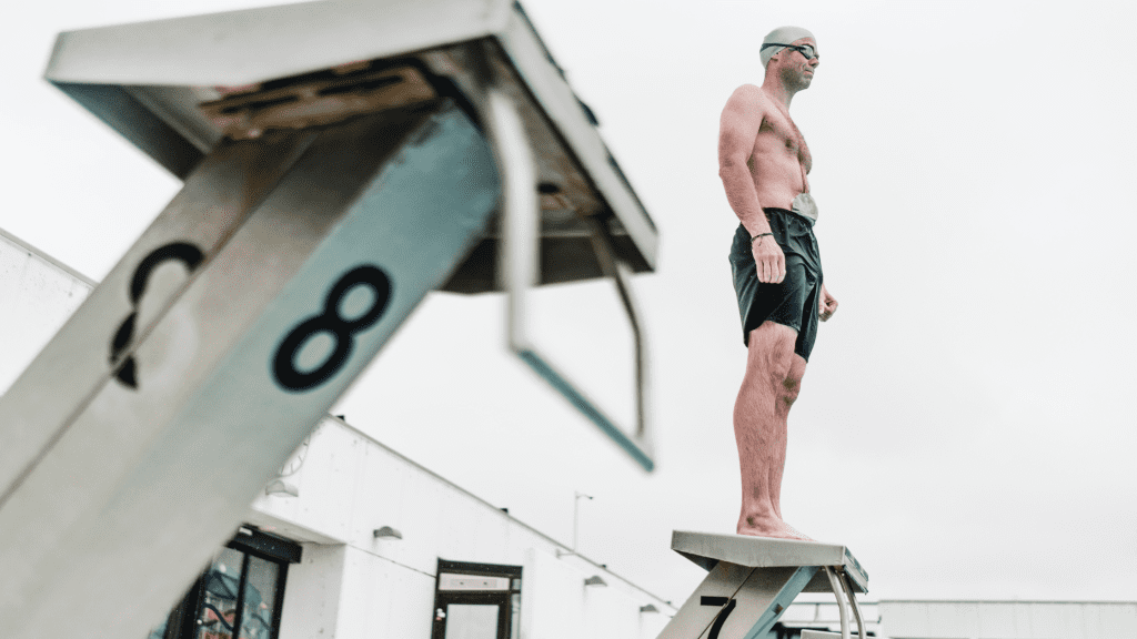 A male with a stoma bag is standing on a diving board.